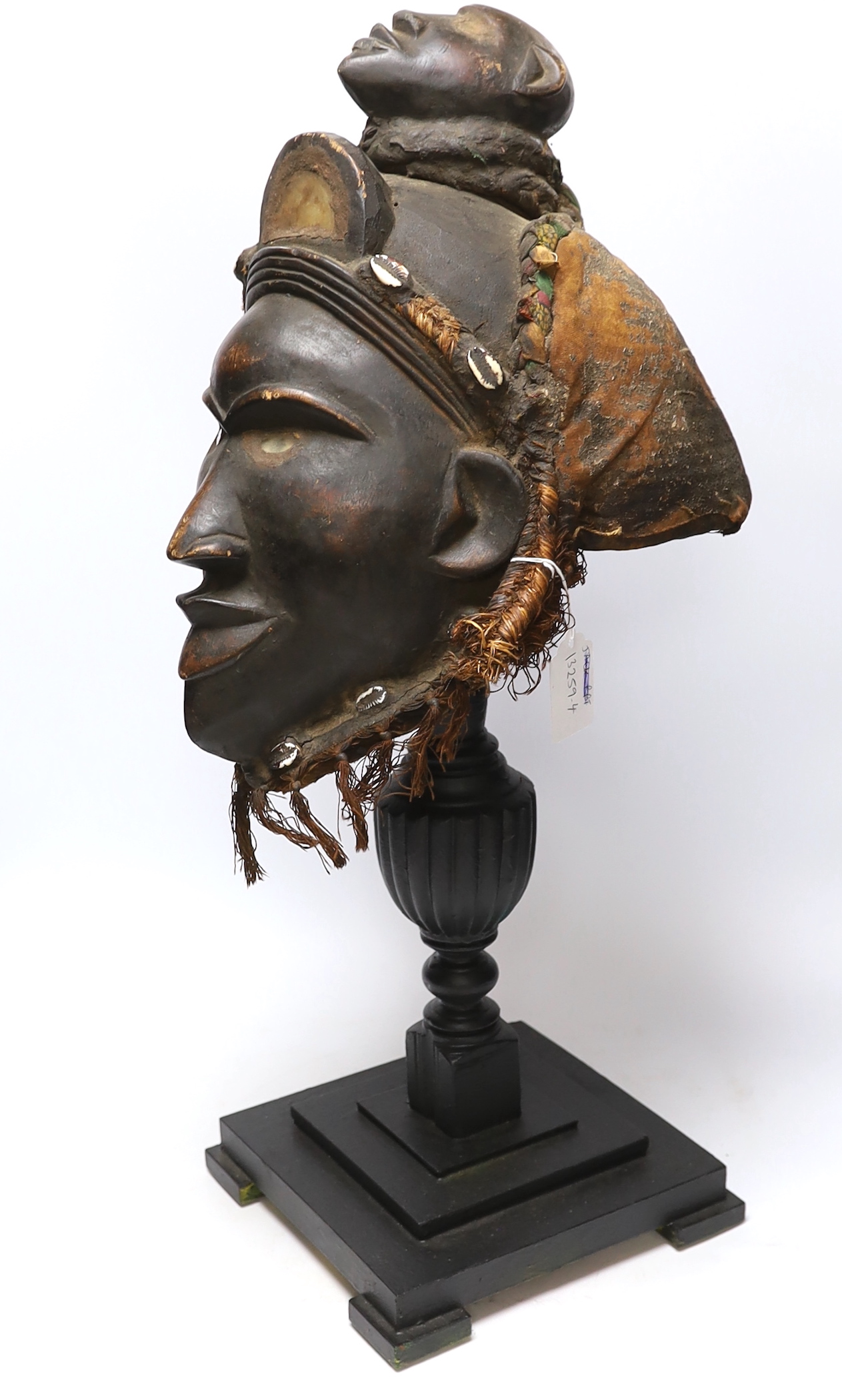 A West African carved wood helmet mask, possibly Kuba (Democratic Republic of Congo), with applied shells and glass inserts, on hardwood stand